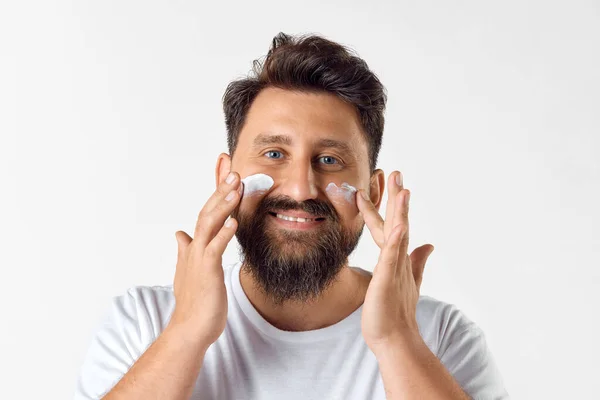满脸胡须 面带微笑 成熟的男人 在白色的工作室背景上 用润肤的面霜呵护肌肤 男性美感 皮肤护理 健康和健康的概念 广告的复制空间 — 图库照片
