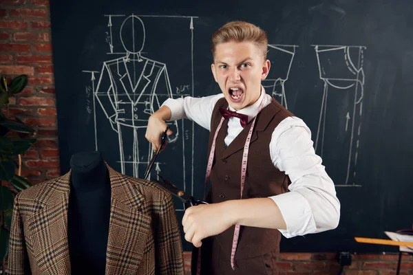 stock image Emotional young man, fashion designer standing with scissors near mannequin with classical suit. Concept of fashion, profession, creativity, occupation, hobby, business