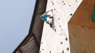 Genç ve sportif bir adam, şortsuz, koruyucu ip ekipmanlarıyla duvara tırmanıyor. Güneşli bir günde açık hava eğitimi. Ekstrem spor, hobi, aktif yaşam tarzı, sağlık ve güç kavramı