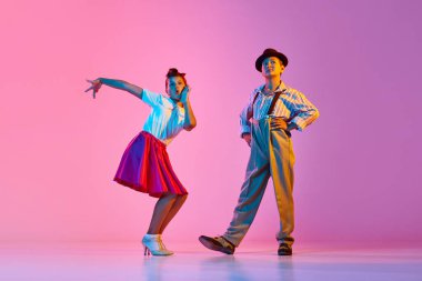 Duygusal, güzel çocuklar, retro kostümlü kız ve erkek neon ışıkta pembe stüdyonun arka planında lindy hop dansı yapıyorlar. Çocukluk kavramı, hobi, aktif yaşam tarzı, performans, sanat, moda
