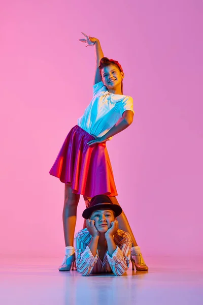 感情的でスタイリッシュな子供たち ネオンライトでピンクのスタジオの背景とレトロダンスを踊る美しい服の男の子と女の子 幼少期 アクティブライフスタイル パフォーマンス アート ファッションの概念 — ストック写真