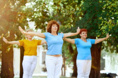 Sunny Morning 'in erken saatlerinde parkta birlikte antrenman yapan yaşlı bir kadın. Antrenman yapıyor, kardiyo egzersizleri yapıyor. Spor ve sağlık kavramı, aktif yaşam tarzı, yaş, sağlık, vücut, bakım