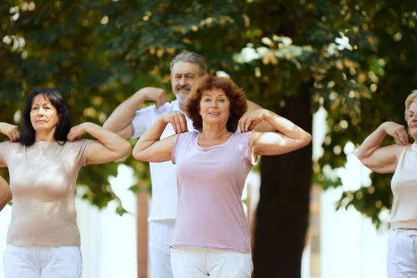 Group of active, elderly people, man and women training outdoors in park, doing warm-up exercises. Concept of sport and health, active lifestyle, age, wellness, body, care