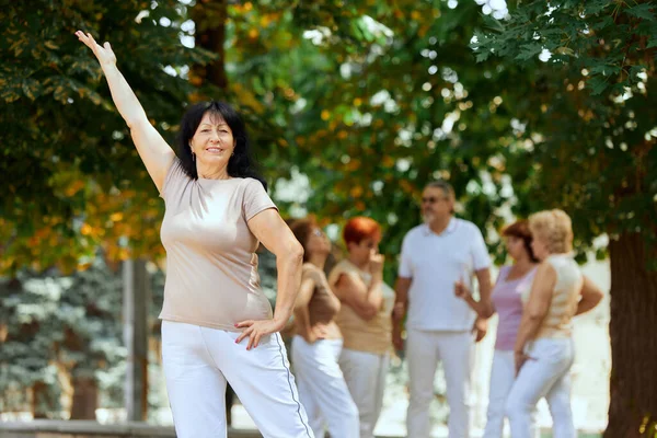 Güneşli bir günde parkta duran son sınıf neşe saçan kadına odaklan. Arka planda bulanık insanlar. Spor ve sağlık kavramı, aktif yaşam tarzı, yaş, sağlık, vücut, bakım