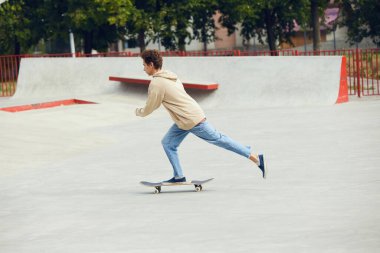 Gündelik giysiler içinde kaykay yapan genç bir çocuk kaykay parkında, açık havada arkadaşlarıyla eğleniyor. Gençlik kültürü, spor, dinamik, aşırı, hobi, eylem ve hareket, arkadaşlık kavramı