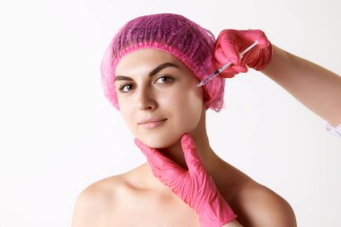 Beyaz stüdyo geçmişine karşı kozmetolojik enjeksiyon yapan genç bir kadın. Kadın güzelliği kavramı, cilt bakımı, kozmetik ve kozmetik, sağlık, estetik cerrahi, reklam