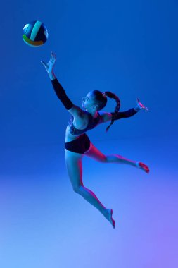 Profesyonel voleybol oyuncusu, hareketli genç bir kadın, neon ışıkta mavi stüdyonun arka planına vuruyor. Profesyonel spor kavramı, rekabet, sağlık, hobi, eylem, reklam