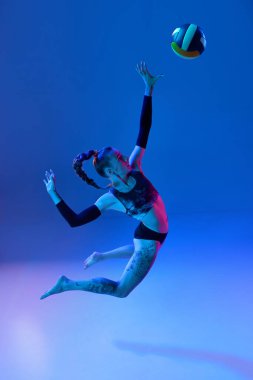 Rekabetçi kız, voleybol oyuncusu neon ışıkta arka planda mavi stüdyoya güçlü bir şekilde vuruyor. Kazanan oyun. Profesyonel spor kavramı, rekabet, sağlık, hobi, eylem, reklam