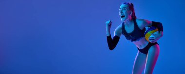 Duygusal ve heyecanlı genç kadın, voleybol oyuncusu mavi arka planda neon ışıkta başarılı oyunu kutluyor. Profesyonel spor, rekabet, sağlık kavramı. Uzayı kopyala. Pankart