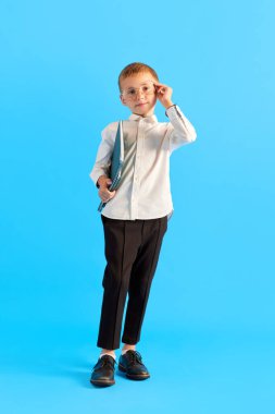 Küçük bir çocuk, gözlüklü, beyaz tişörtlü ve siyah pantolonlu mavi stüdyo arka planında klasörleri olan bir çocuk. Akıllıca. Çocukluk kavramı, eğitim, okul, çocuk duyguları, reklam