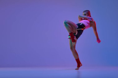 Atletik genç kızın dinamik fotoğrafı, spor giyimli anne dövüşçüsü neon ışıklarda mor arka planda. Karışık dövüş sanatları, spor, hobi, rekabet, atletizm, güç ve reklam kavramı