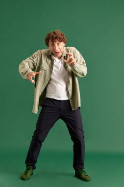 Yeşil stüdyo arka planında garip, tuhaf, suratını buruşturan normal giyinmiş olgun bir adam. İnsan duyguları kavramı, yüz ifadesi, yaşam tarzı, moda, reklam