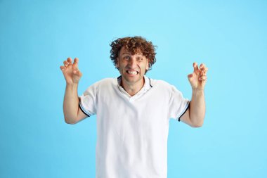 Sıradan beyaz tişörtlü kıvırcık adam mavi stüdyo geçmişine karşı öfke ve asabiyet gösteriyor. Tatsız bir durum. İnsan duyguları, yüz ifadesi, yaşam tarzı kavramı