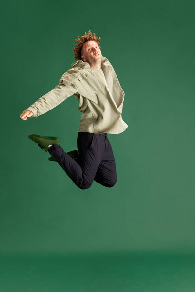 Зрелый мужчина в повседневной одежде эмоционально прыгает на фоне зеленой студии. Новости, продажи, сюрприз. Концепция человеческих эмоций, выражение лица, образ жизни, мода, реклама