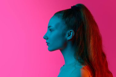 Profil görüntüsü, sakin, duygusuz bir yüzle neon ışıkta pembe stüdyonun arka planına bakan genç bir kız. İnsan duyguları kavramı, moda, güzellik, yaşam tarzı, gençlik, reklam
