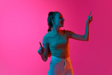 Genç kız, işçi, görünmez ekrana dokunan öğrenci, neon ışıkta pembe stüdyonun arka planına karşı öncü sunum. İnsan duyguları kavramı, moda, güzellik, yaşam tarzı, gençlik, reklam