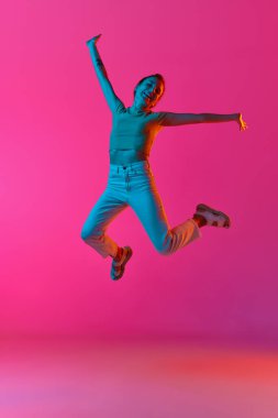 Başarı ve mutluluk. Heyecanlı ve duygusal genç kadın neon ışıkta pembe stüdyo geçmişine neşeyle zıplıyor. İnsan duyguları kavramı, moda, güzellik, yaşam tarzı, gençlik, reklam
