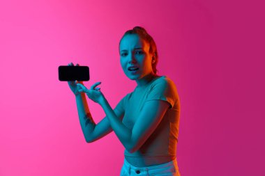 Şüpheli, sorgulayıcı yüzü olan genç bir kız cep telefonu ekranında, neon ışıkta pembe stüdyonun arka planına bakıyor. İnsan duyguları kavramı, sosyal medya, satış, yaşam tarzı, gençlik, reklam