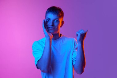 Heyecanlı gülümseyen genç bir adam sırlarını fısıldıyor ve neon ışıklarındaki pembe arkaplanı yan gösteriyordu. İnsan duyguları kavramı, gençlik, yaşam tarzı, moda, satış, reklam