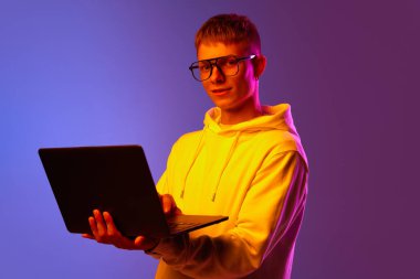 Genç bir adam, gözlüklü bir öğrenci dizüstü bilgisayarla neon ışıkta mor renge karşı duruyor. Serbest çalışıyorum. İnsan duyguları kavramı, gençlik, yaşam tarzı, iş, eğitim, reklam