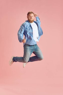 Uzun boylu, sakallı olgun bir adamın gündelik kıyafetleri içinde pembe stüdyo arka planında duygusal olarak zıplayıp bağırışları. İnsan duyguları kavramı, yaşam tarzı, yüz ifadesi, reklam. İlan için alanı kopyala