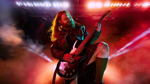 Rock and roll concert. Artistic, expressive man with long hair playing guitar and making performance, emotionally singing. Concept of music, performance, art, talent, nightlife, joy, party, lifestyle