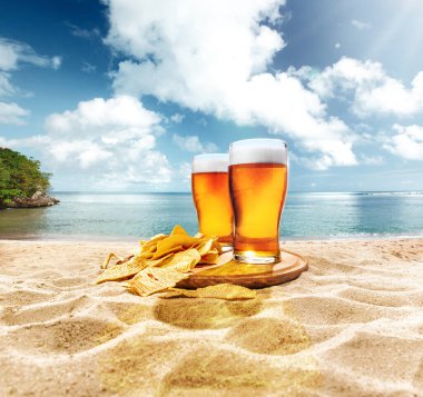 İki bardak köpüklü, soğuk, bira patates kızartmalı aperatifler kumda okyanusa ve mavi gökyüzüne karşı. Bira, bira fabrikası, tatil ve tatil kavramı, gelenekler, festival, alkol içeceği, reklam