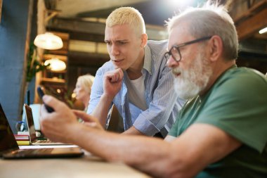Modern ofiste çalışan genç ve kıdemli bir adam projeler ve stratejiler hakkında konuşuyor. Zorluklar. İş kavramı, yaş çeşitliliği, eğitim, modernlik, yenilikler, yardım