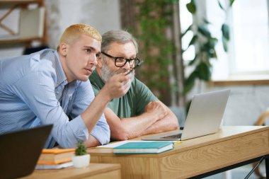 Genç bir adam, kıdemli biriyle çalışan ve onunla iş denklemlerini tartışan. Yardım ve işbirliği. İş kavramı, yaş çeşitliliği, eğitim, modernlik, yenilikler, tartışma