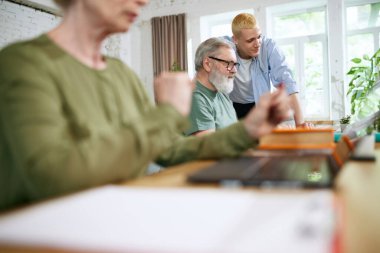 Çalışanlar arasındaki profesyonel işbirliği. Genç adam ve kıdemli iş adamları birlikte çalışıyor, görevleri çözüyor, yeni şeyler öğreniyor ve öğretiyorlar. İş kavramı, eğitim, yenilikler, yardım