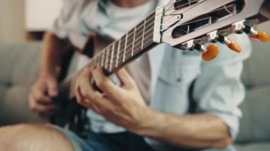 Elektro gitar çalan erkek ellerinin yakın çekimi. Kanepede oturan ve yeni şarkılar öğrenen gündelik elbiseli bir adam. Müzik kavramı, hobi, yaratıcı yaşam tarzı, eğitim, eğlence, performans