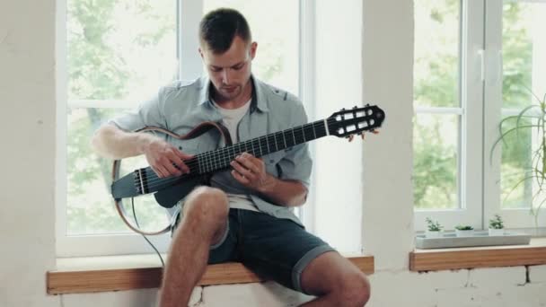 Junger Mann Sitzt Tagsüber Fenster Und Spielt Gitarre Zeit Für — Stockvideo
