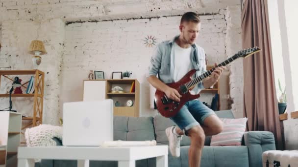 穿着休闲装的年轻而情绪化的男人在客厅里呆着 弹吉他 业余爱好 创意生活方式 表演的概念 — 图库视频影像