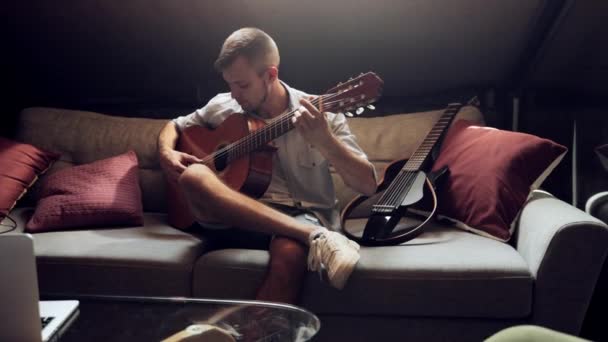 阁楼的内部 年轻男子坐在阁楼沙发上 晚上舒舒服服地弹吉他 享受快乐 业余爱好 创意生活方式 表演的概念 — 图库视频影像