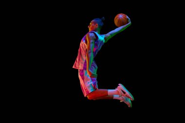 Atletik genç adam, maç sırasında hareket eden basketbol oyuncusu, neon ışıkta siyah stüdyonun arka planına karşı top ile zıplıyor. Profesyonel spor, rekabet, hobi, oyun, rekabet kavramı