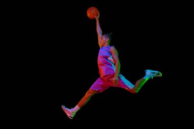 Smaç basıldı. Kazanan gol. Basketbol oynayan genç bir çocuk, neon ışıkta siyah stüdyonun arka planına karşı top fırlatıyor. Profesyonel spor, rekabet, hobi, oyun, rekabet kavramı