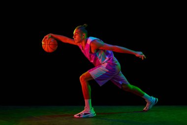 Kaslı, hareketli genç bir adam, neon ışıkta siyah arka planla maç sırasında basketbol oynayan bir basketbolcu. Profesyonel spor kavramı, rekabet, hobi, aktif yaşam tarzı, rekabet