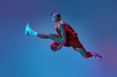 Genç sporcu, hareketli basketbolcu topla neon ışıkta mavi stüdyonun arka planına zıplıyor. Profesyonel spor, rekabet, hobi, oyun, rekabet kavramı