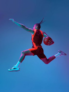 Rekabetçi ruh. Atletik genç erkek antrenmanı, neon ışıkta mavi stüdyonun arka planında basketbol oynamak. Profesyonel spor, rekabet, hobi, oyun, rekabet kavramı