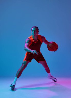 Top sürüyorum. Üniformalı genç bir çocuğun dinamik görüntüsü, mavi ışıkta arka planda basketbol oynuyor. Profesyonel spor, rekabet, hobi, oyun, rekabet kavramı