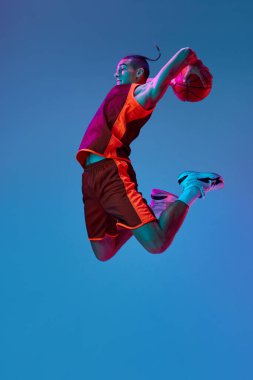 Rekabetçi ruh. Atletik genç erkek antrenmanı, neon ışıkta mavi stüdyonun arka planında basketbol oynamak. Profesyonel spor, rekabet, hobi, oyun, rekabet kavramı