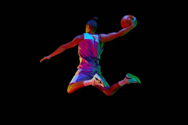 若い男のバックビュー画像 スポーツウェアトレーニングのバスケットボールプレーヤー ネオンライトのブラックスタジオの背景にジャンプして投げる スポーツ ゲーム コンテスト — ストック写真