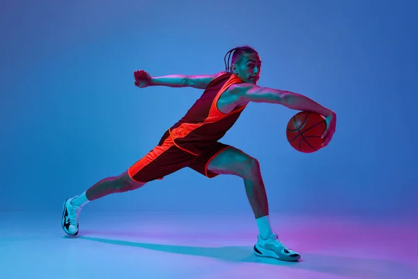バスケットボールをするスポーツウェアに興味を持った若者は ネオンライトの青いスタジオの背景でボール演習をトレーニングします プロスポーツ ゲーム 競技のコンセプト — ストック写真