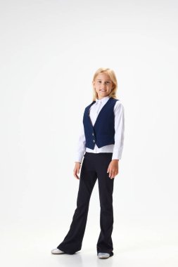 Güzel liseli kızın tam boy portresi, şık üniformalı bir çocuk beyaz stüdyo arka planında gülümseyerek ayakta duruyor. Çocukluk kavramı, okul, eğitim, moda, tarz. İlan için alanı kopyala
