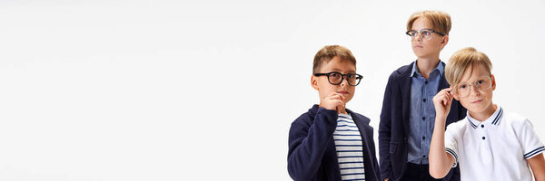 Children, boys, classmates in stylish school uniform and glasses standing against white studio background. Concept of childhood, school, education, fashion, style. Copy space for ad. Banner