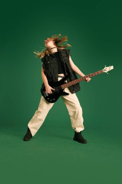 Yeşil stüdyo arka planında duygusal olarak elektro gitar çalan şık elbiseli genç bir kız resmi. Müzik kavramı, insani duygular, gençlik, moda, yaşam tarzı, reklam