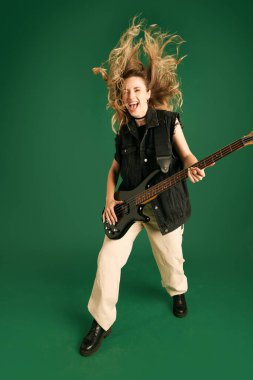 Yeşil stüdyo arka planında duygusal olarak elektro gitar çalan şık elbiseli genç bir kız resmi. Müzik kavramı, insani duygular, gençlik, moda, yaşam tarzı, reklam