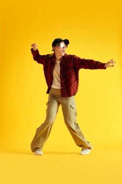 Şık giyinmiş, dans eden ve sarı stüdyo arka planında eğlenen genç bir kadının tam boy görüntüsü. Hippi. İnsan duyguları kavramı, gençlik, moda, yaşam tarzı, reklam