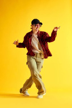 Şık giyinmiş, dans eden ve sarı stüdyo arka planında eğlenen genç bir kadının tam boy görüntüsü. Hippi. İnsan duyguları kavramı, gençlik, moda, yaşam tarzı, reklam