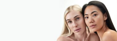 İki güzel genç kadın, beyaz arka planda kameraya bakan, beyaz tenli ve Asyalı. Çok ırklı güzellik anlayışı, spa, kozmetoloji, sağlık. Pankart. İlan için alanı kopyala